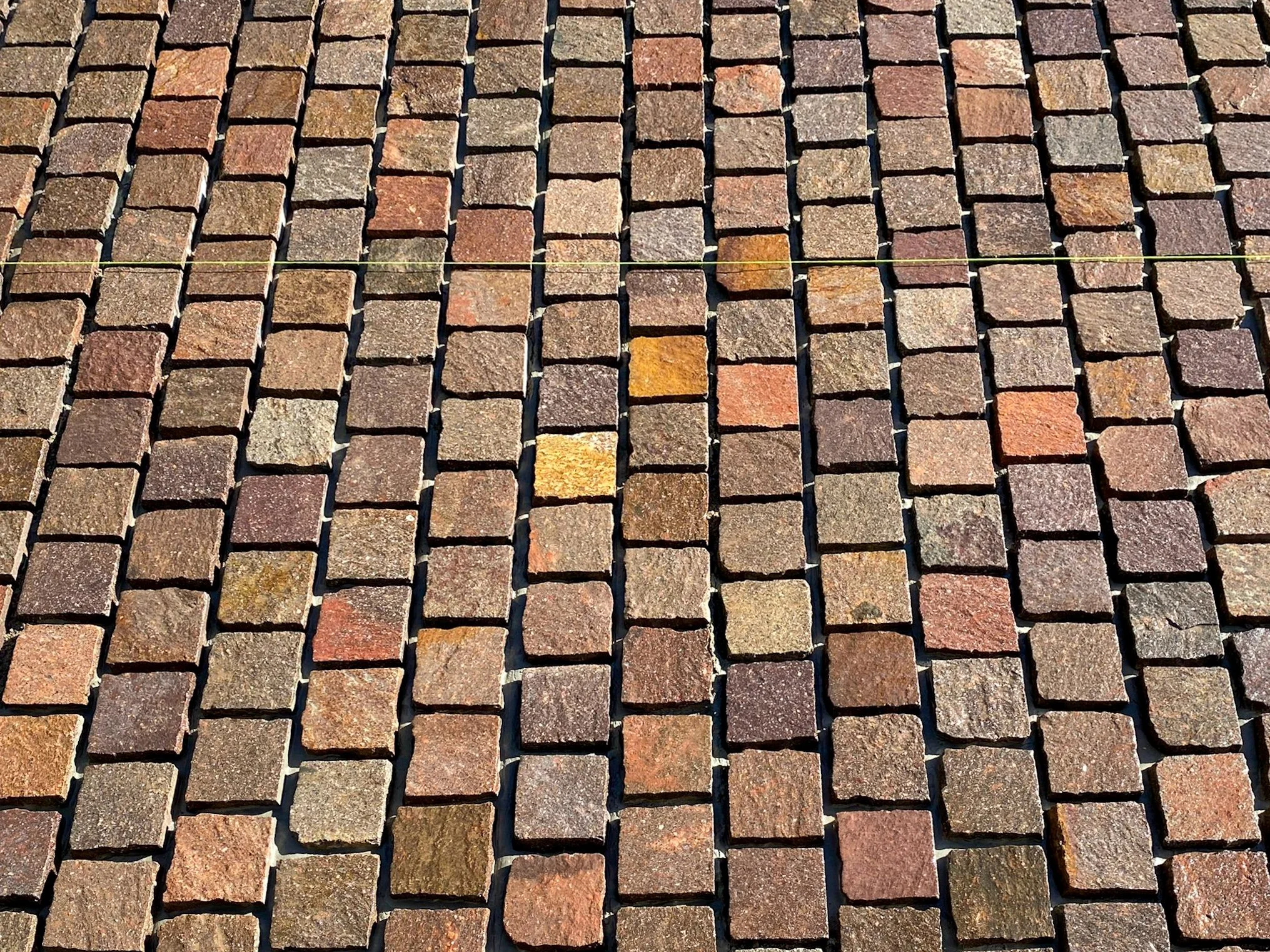 Close-up view of a cobblestone pavement with rectangular stones arranged in a grid pattern, featuring various shades of brown, red, and tan.