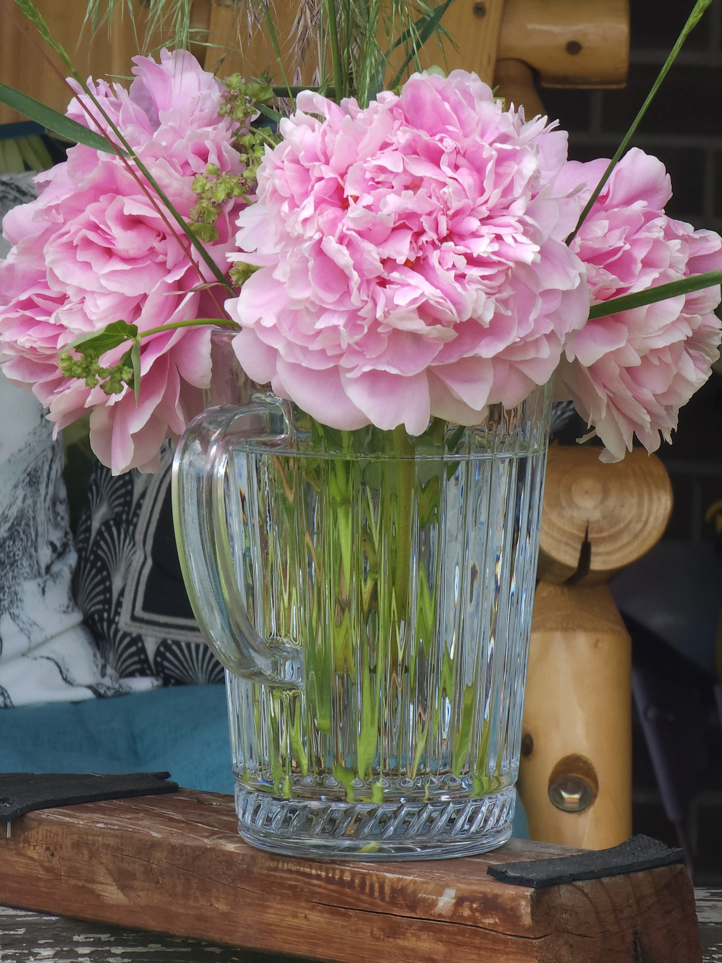 Pink peony flowers in a clear glass vase on a wooden surface.