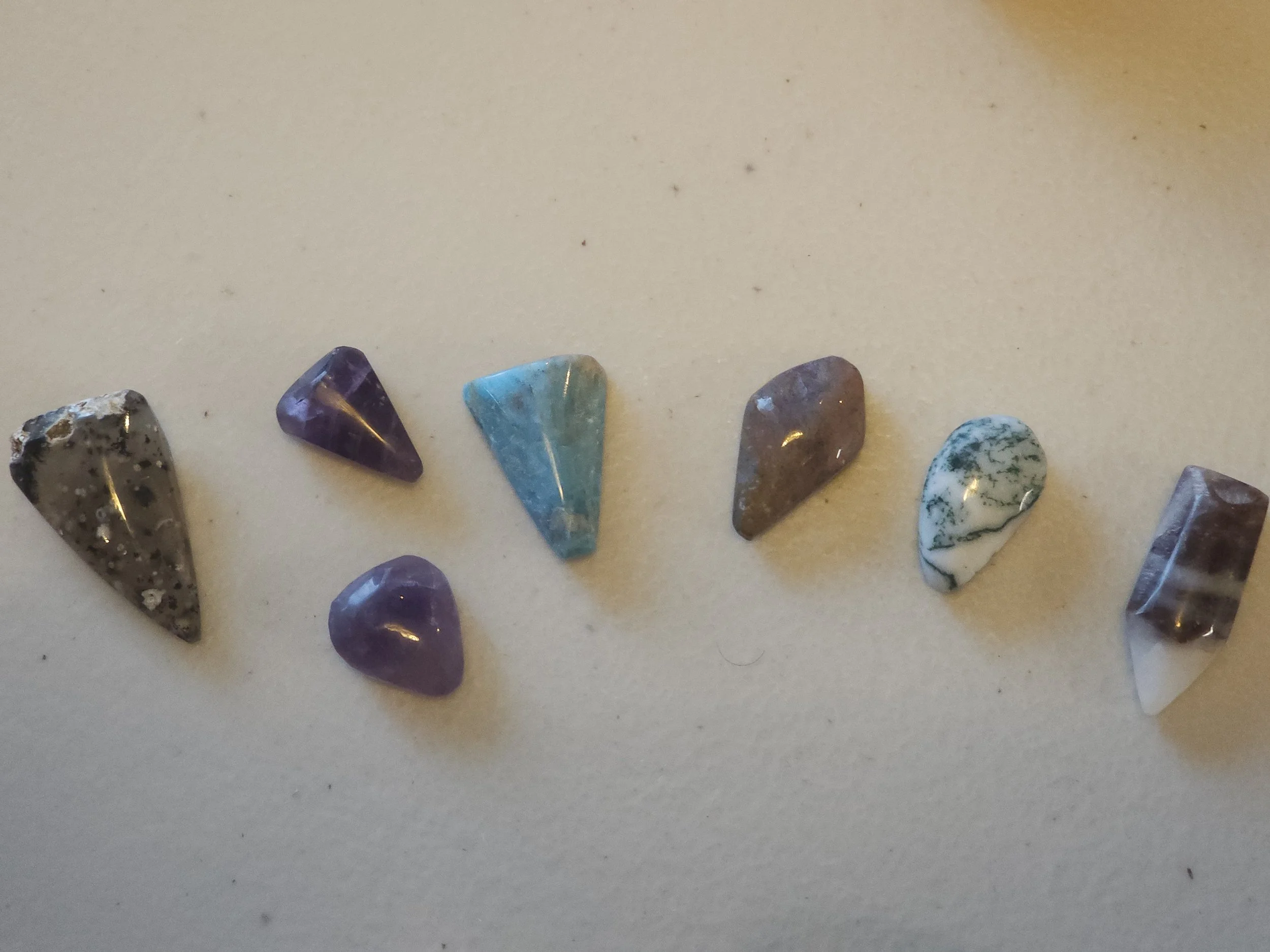 Eight tumbled semi-precious stones of various colors and patterns arranged in a row on a white surface.