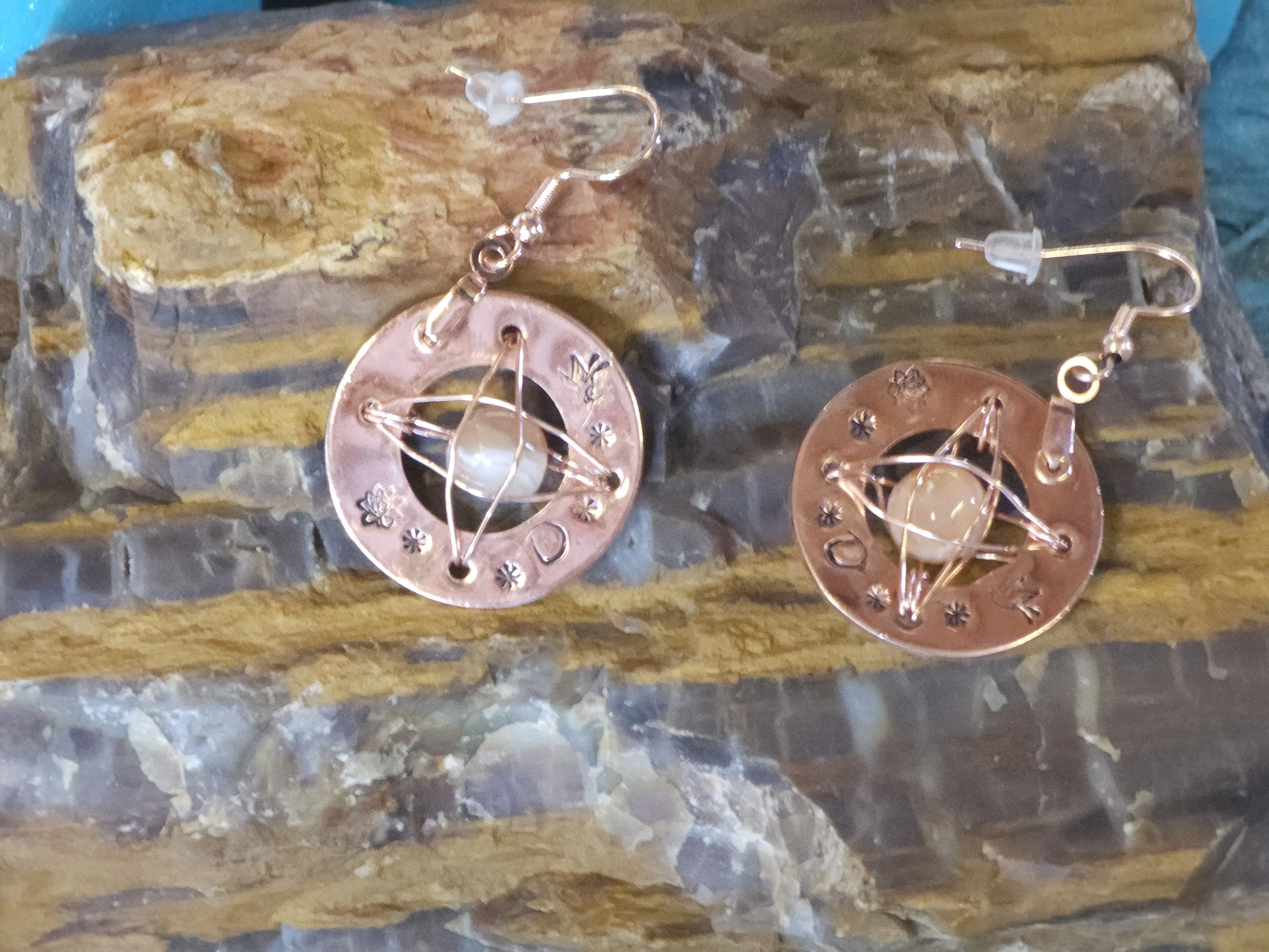A pair of circular earrings with hand stamped details wire wrapped, placed on petrified wood.