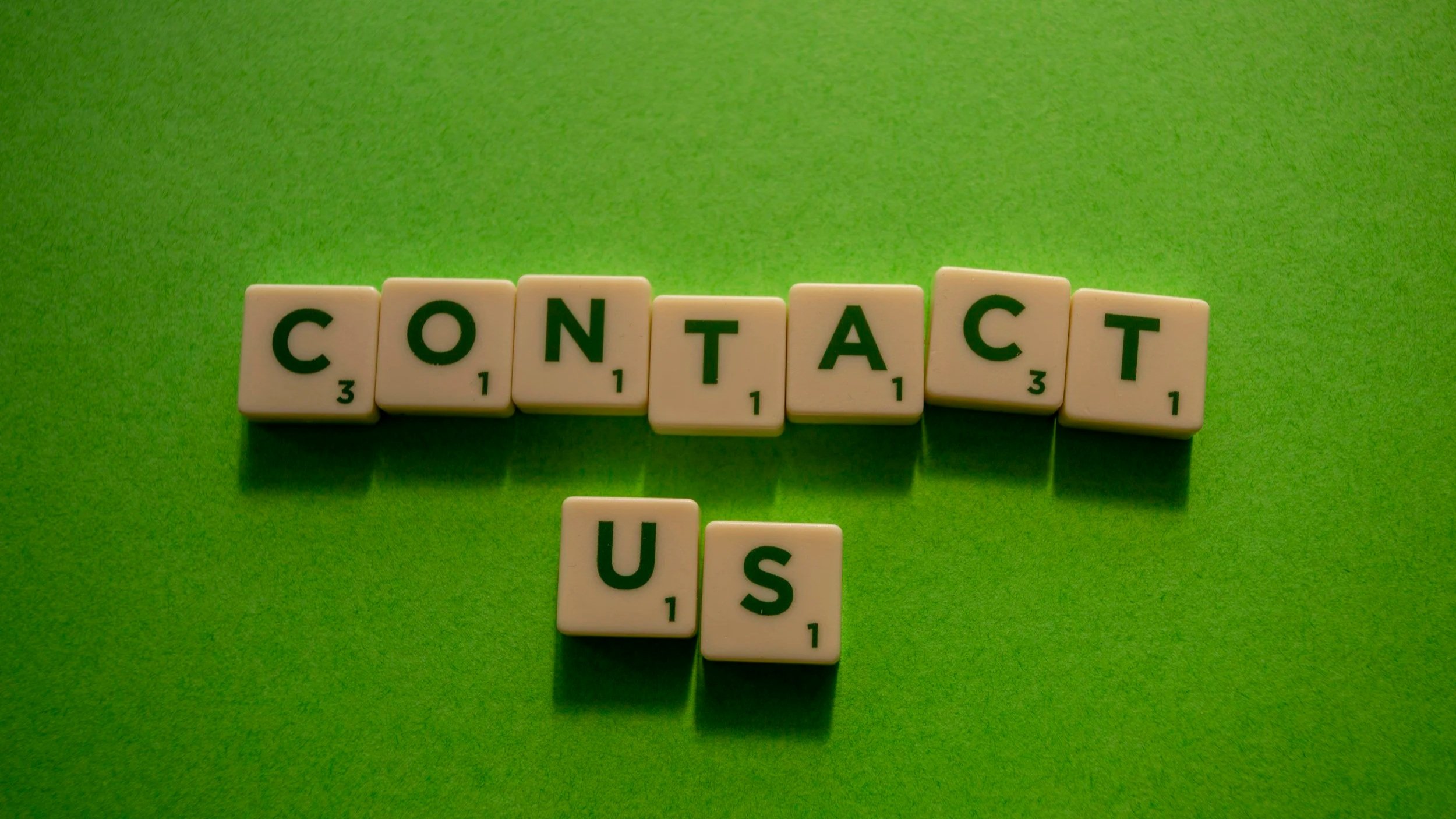 Scrabble tiles spelling out 'CONTACT US' on a green background.