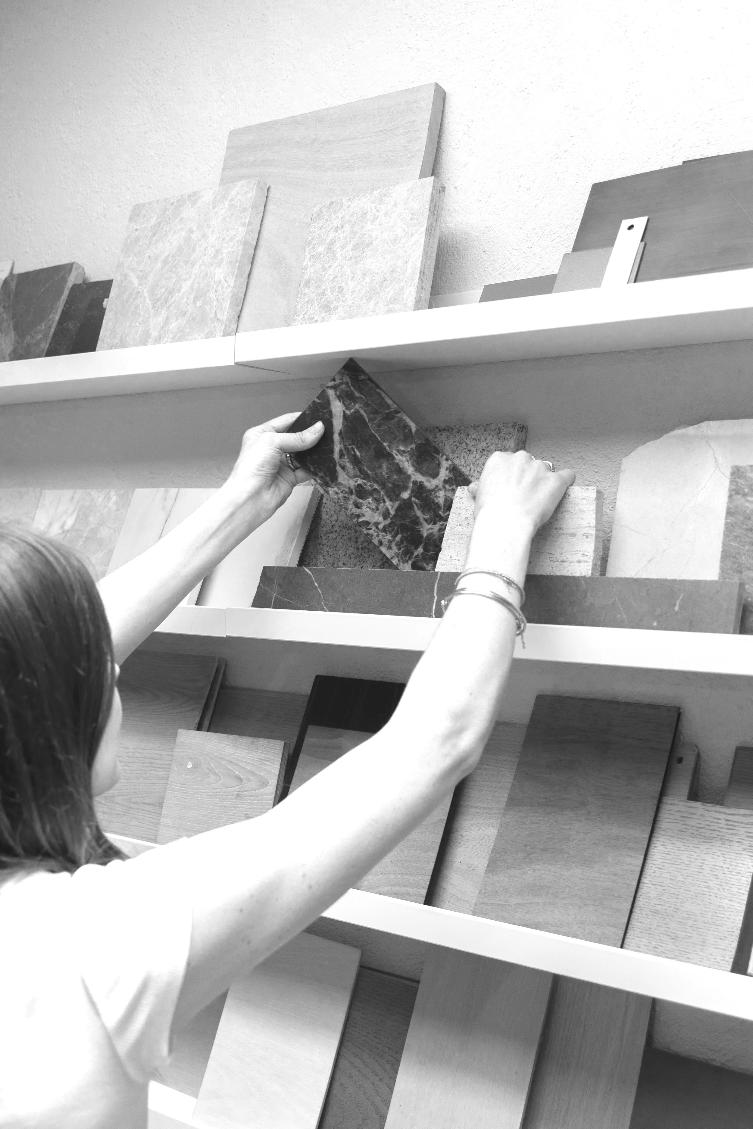 A person selecting a marble tile from a showroom display, with various tiles on shelves.