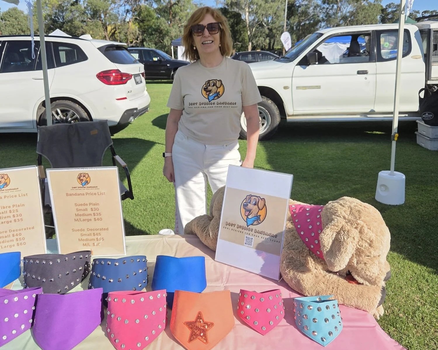 The owner of Best Buddies Bandanas owner Jackie wearing a Best Buddies Bandanas shirt at her booth at a dog market, along with colourful dog accessories in the form of dog bandanas.
