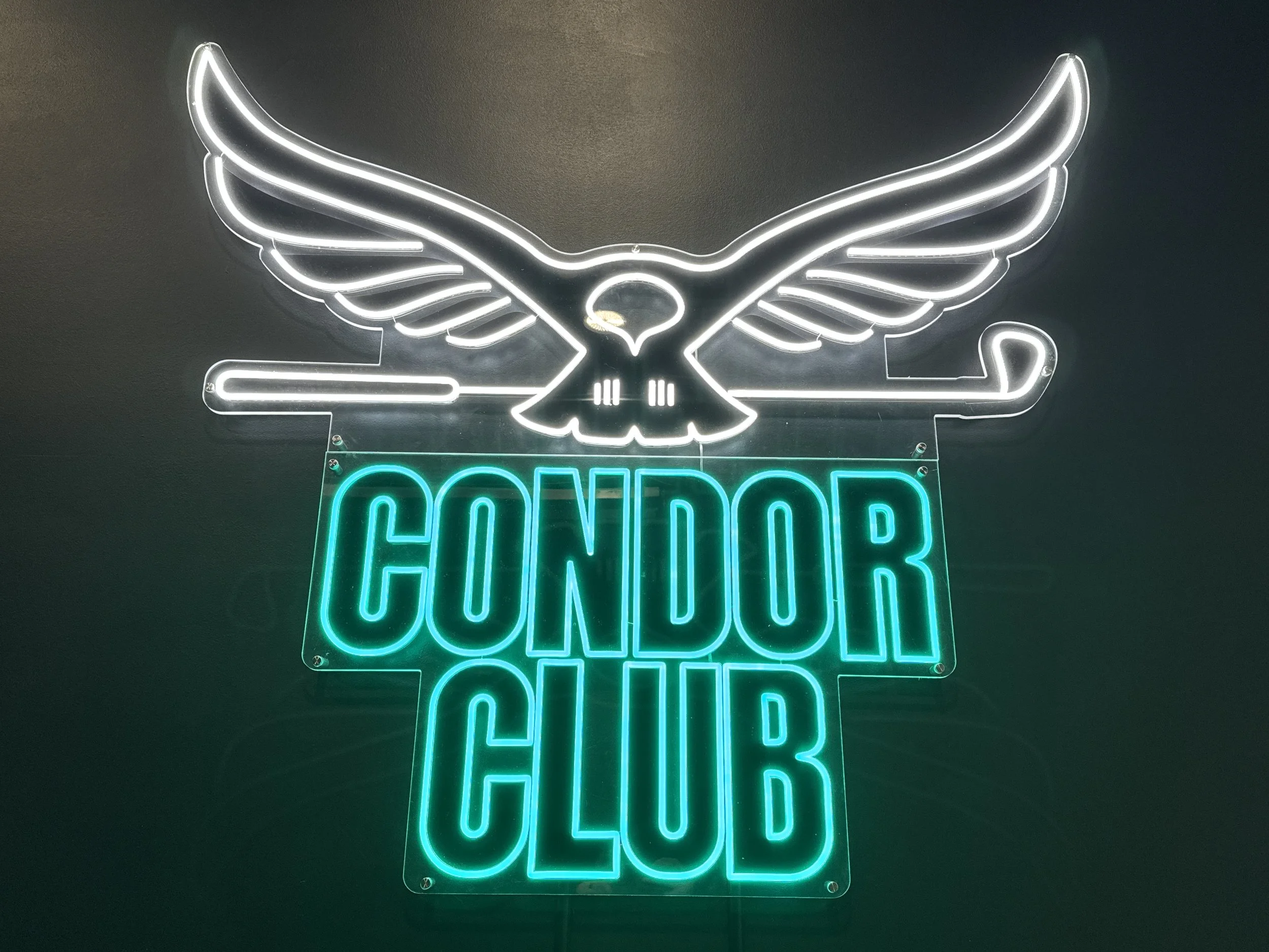 Neon sign of a bird with outstretched wings above the words "CONDOR CLUB" in bright teal.