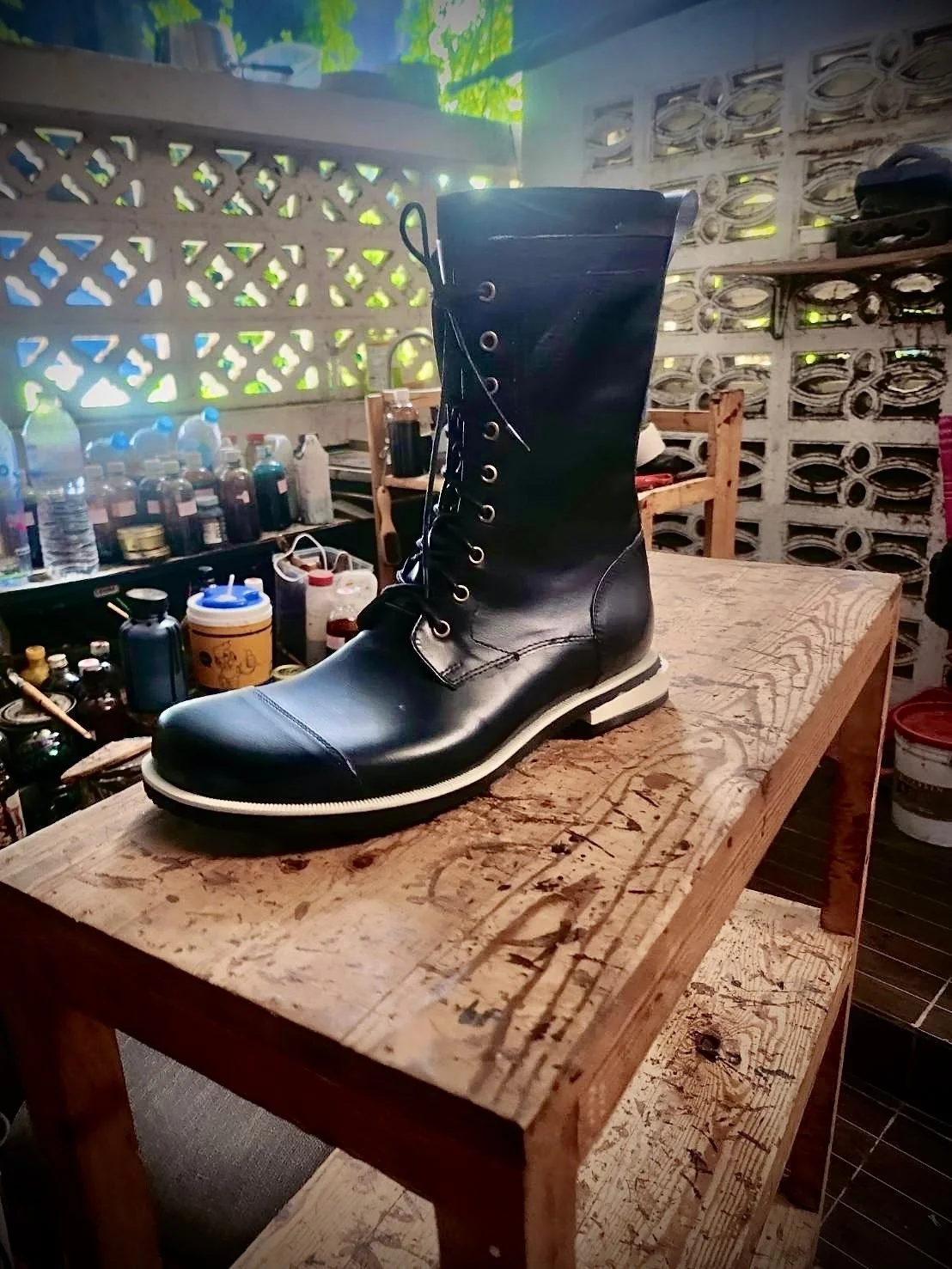 Black minimalist adventure boot placed on wooden workbench in a workshop with bottles and jars in the background