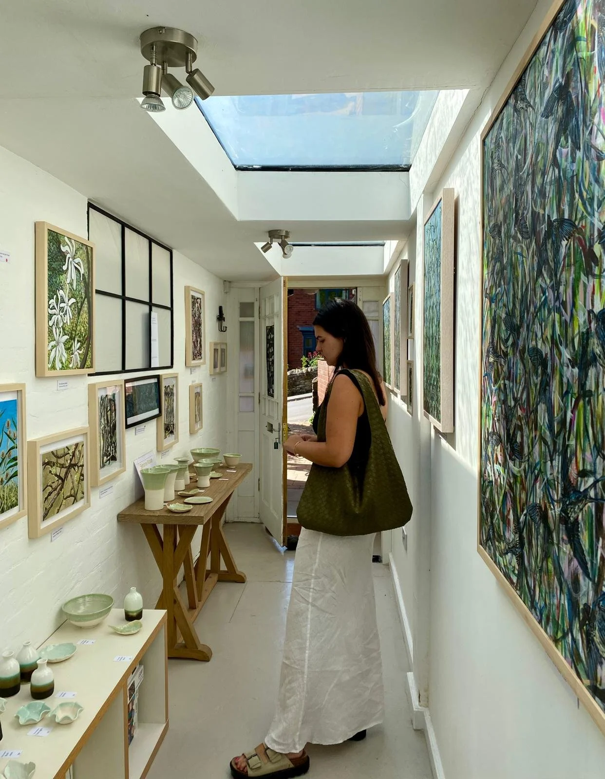A woman shopping for pottery in an art gallery with paintings on the wall and pottery on tables.