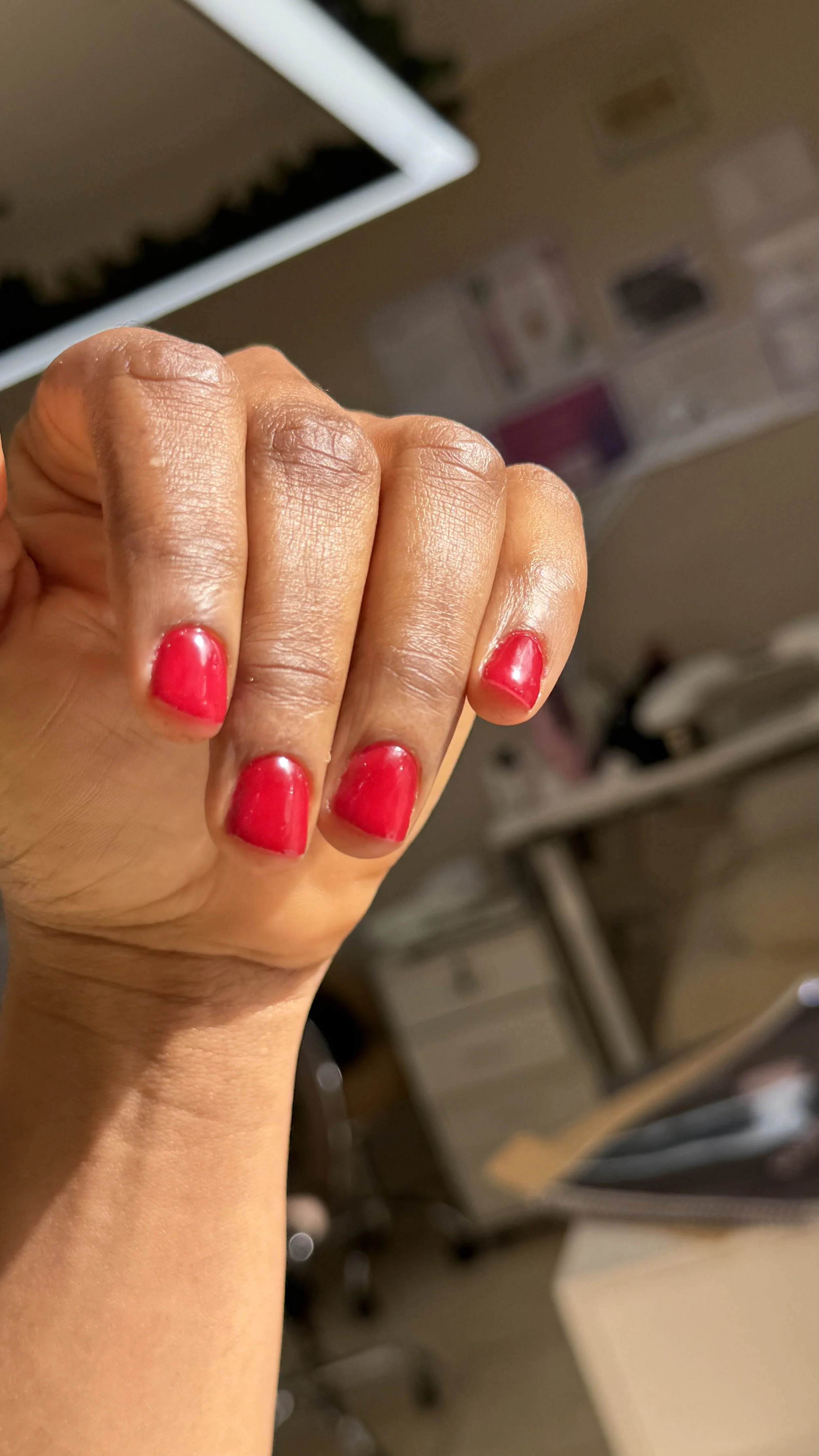 Close-up of a person's hand showing freshly painted red fingernails in an indoor setting with blurred background.