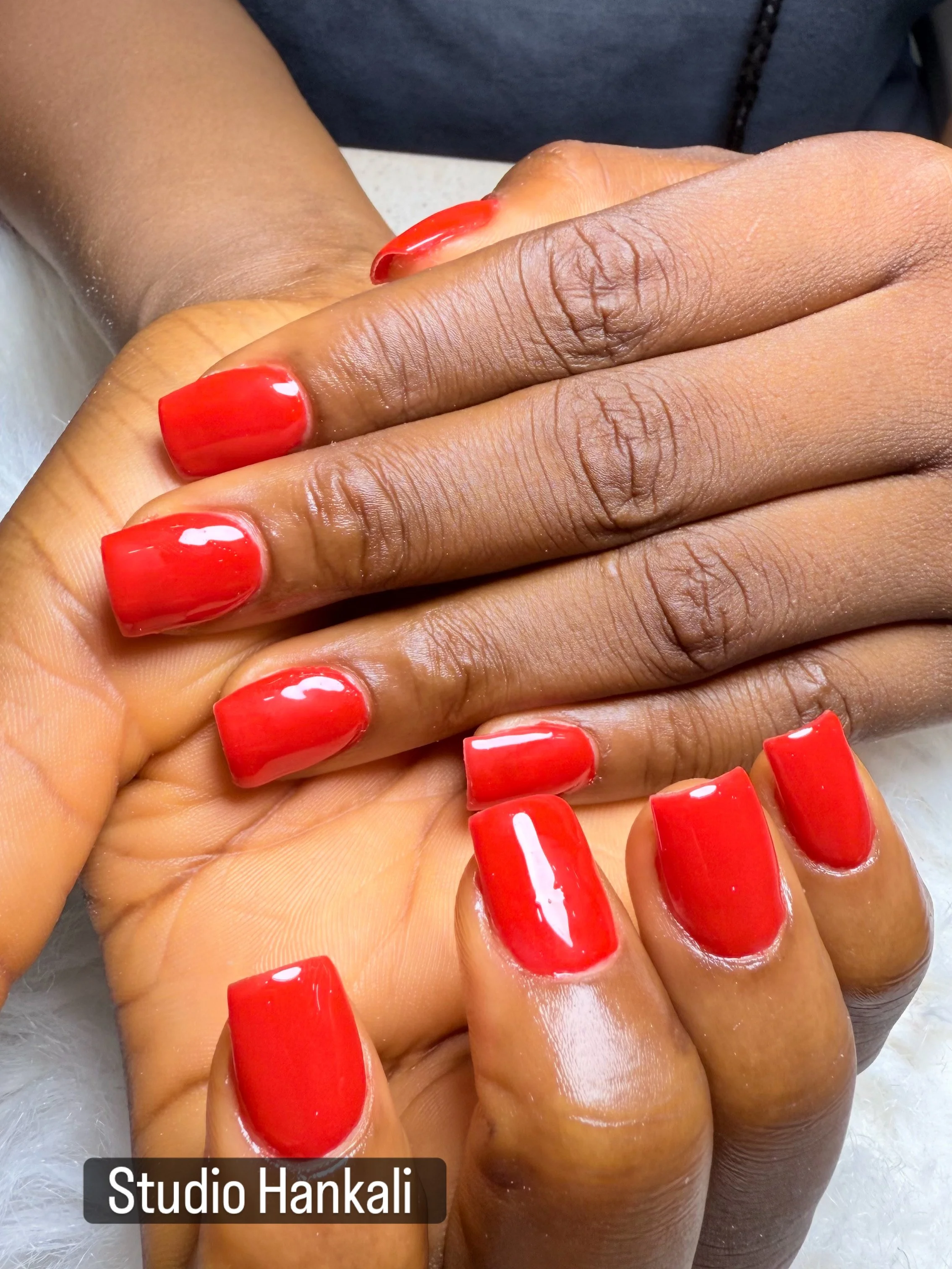 Close-up of two hands with freshly manicured nails painted in bright red. The image indicates a professional manicure session at Studio Hankali.