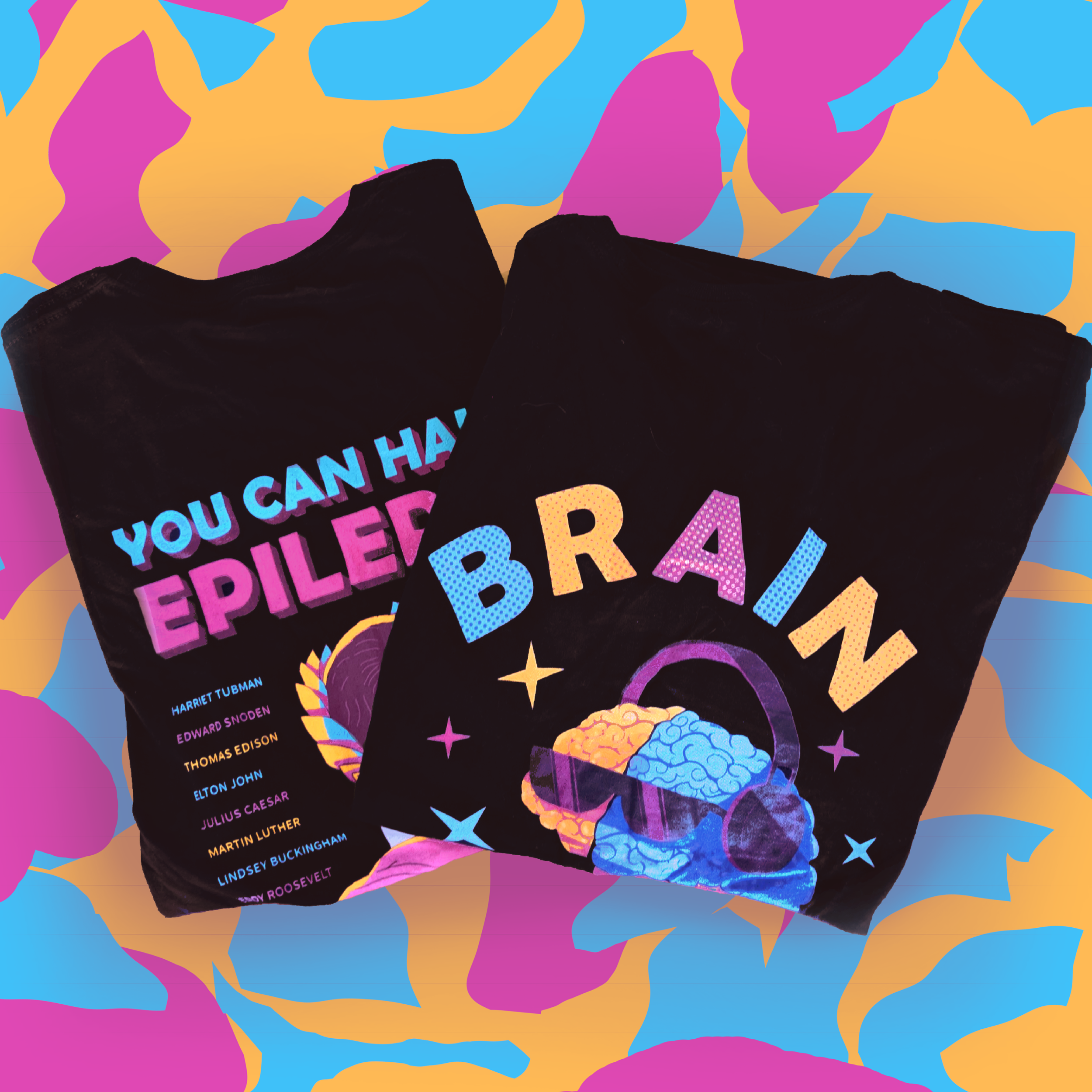 Two black T-shirts with colorful text and graphics, one displaying the word "BRain" with a brain wearing sunglasses and the other with a list of historical figures under the heading "You Can Have Epilepsy." The background features an abstract pattern of pink, purple, blue, and orange shapes.