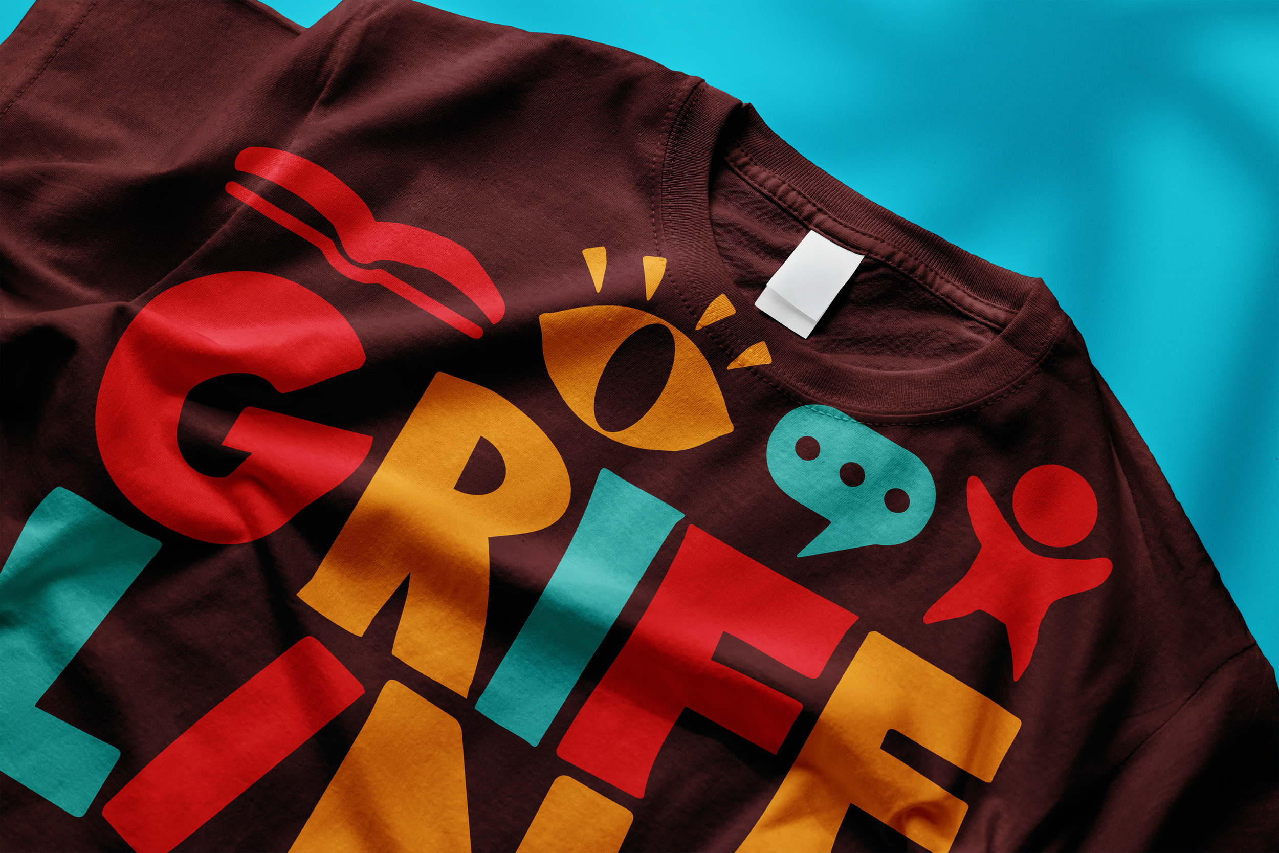 Colorful T-shirt with playful graphic design, including a red hand, a yellow sun, speech bubbles, and a red star against a blue background.