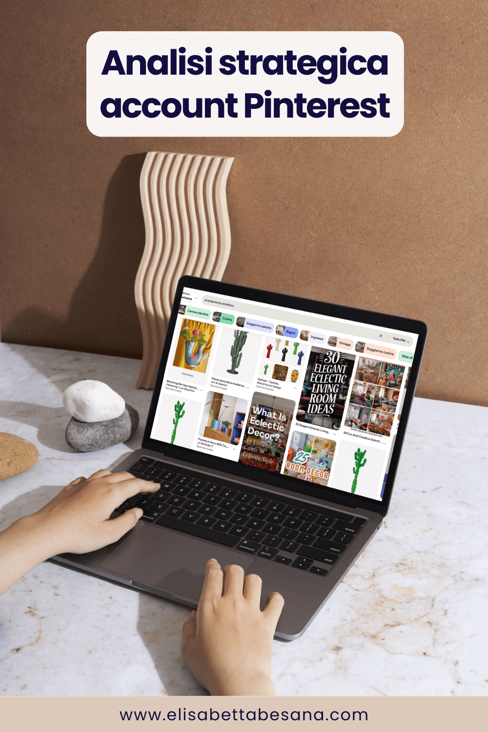 foto di laptop aperto con schermata su feed di pinterest, poggiato su tavolo di marmo chiaro, parete marrone