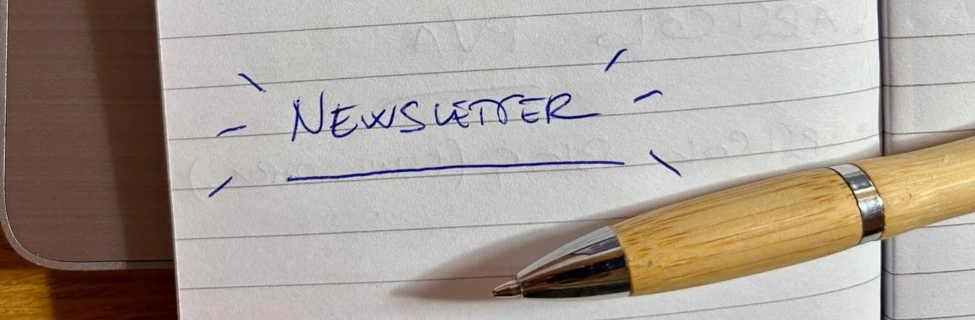 Immagine orizzontale, foglio a righe con scritto a penna in blu Newsletter, penna poggiata sopra
