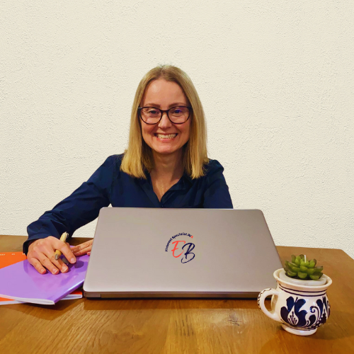 donna capelli lisci e biondi, con occhiali da vista, seduta alla scrivania con laptop grigio