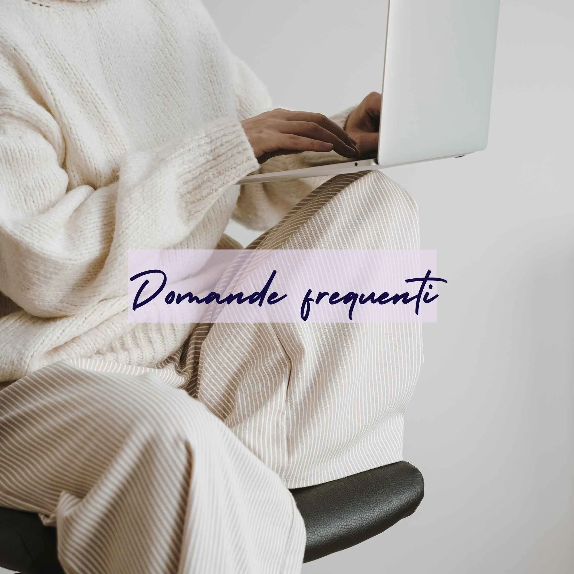 donna vestita di maglia e pantaloni bianchi seduta su uno sgabello mentre lavora al laptop.