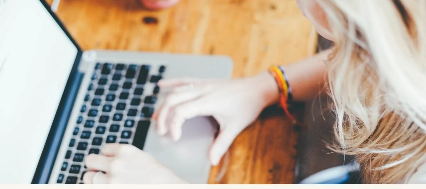 immagine sfocata di un laptop su tavolo di legno, si intravede una donna bionda che lavora al computer. Scopri come costruire un sales funnel su Pinterest.