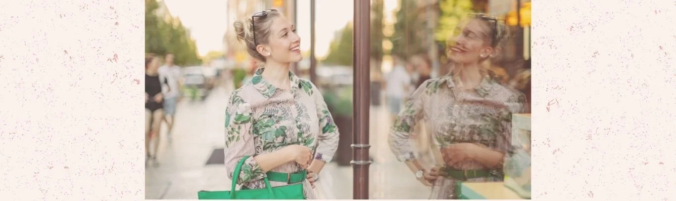 giovane donna sorridente che si ferma a guardare una vetrina con aria convinta e soddisfatta.