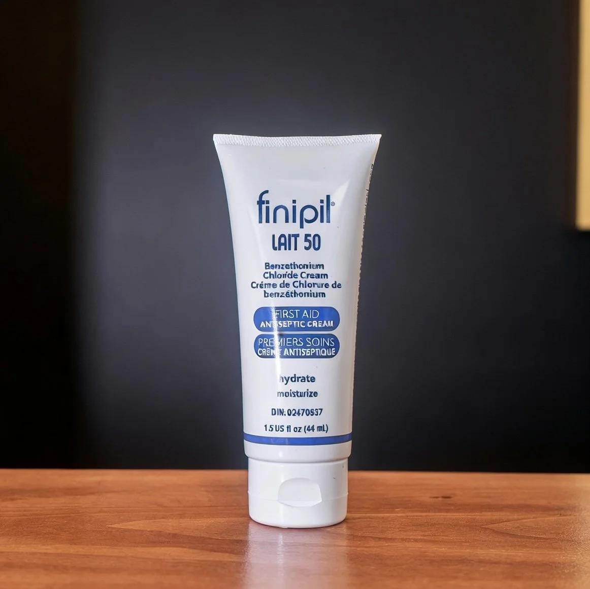 A white tube of finipil LAIT 50 Benzethonium Chloride Cream on a wooden surface with a dark background.