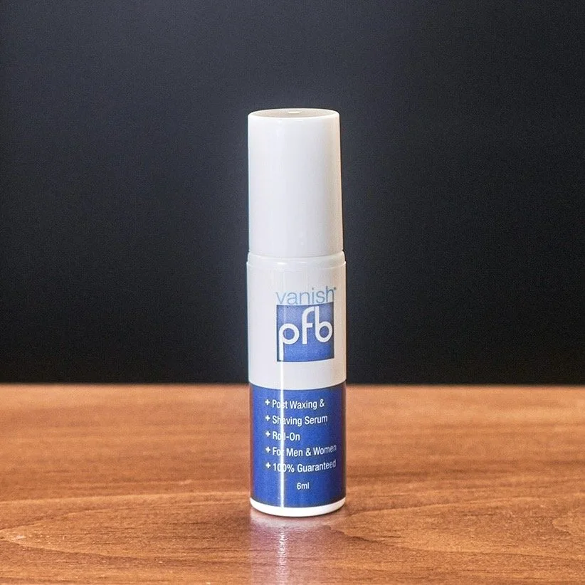 A small white and blue bottle of PFB vanish post waxing and shaving serum on a wooden surface against a black background.