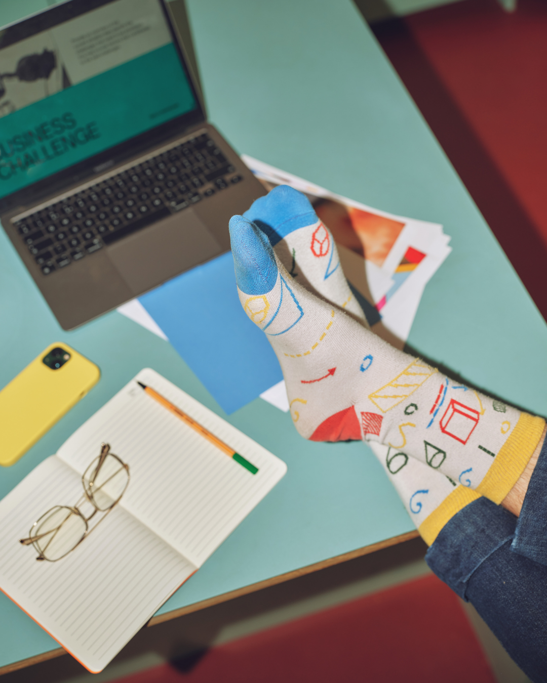 Bureau avec un ordinateur. Une personne a ses pieds croisés sur le bureau. Cette personne a des bas très colorés.