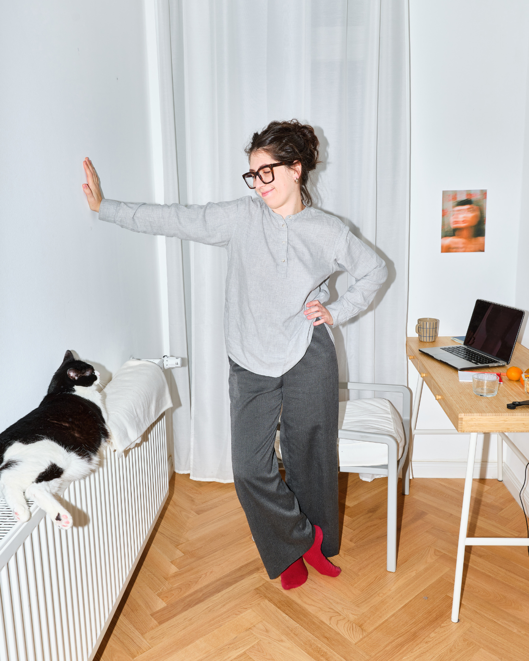 Femme debout à côté de son bureau où il y a un ordinateur, elle regarde son chat qui est couché sur le système de chauffage