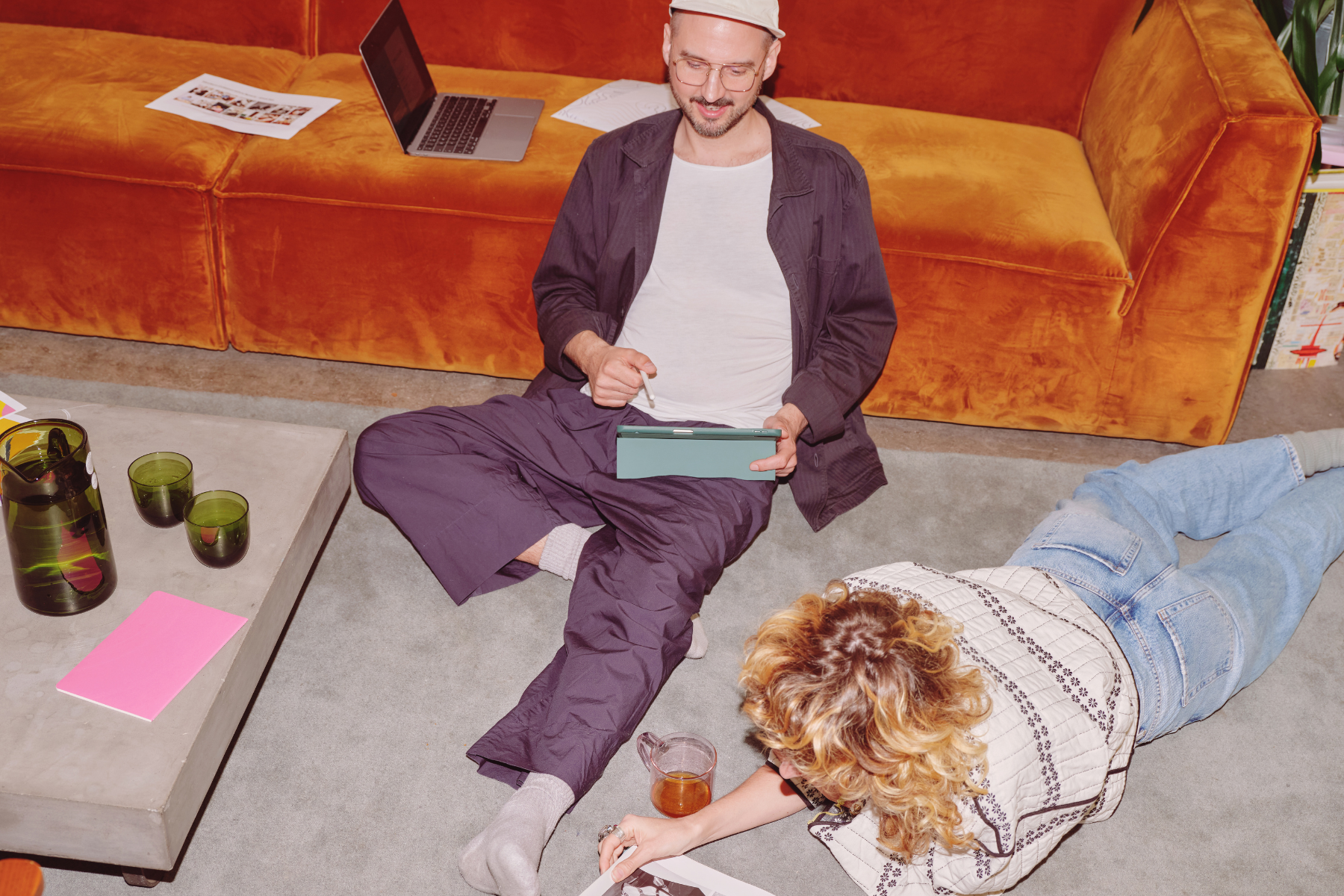 Deux adultes assis par terre dans un salon qui navigue sur une tablette et un ordinateur