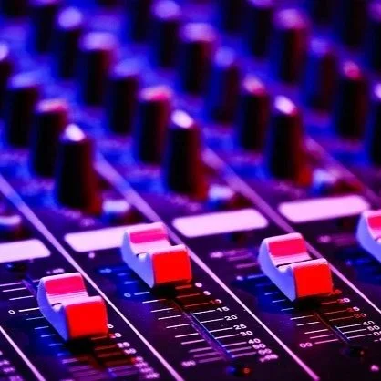 Close-up of a professional audio mixing console with illuminated sliders and controls.