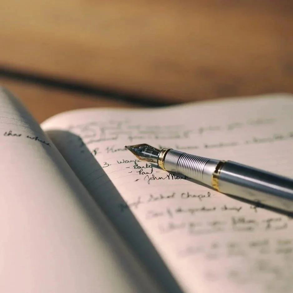 Close-up of a silver fountain pen resting on an open notebook with handwritten notes.