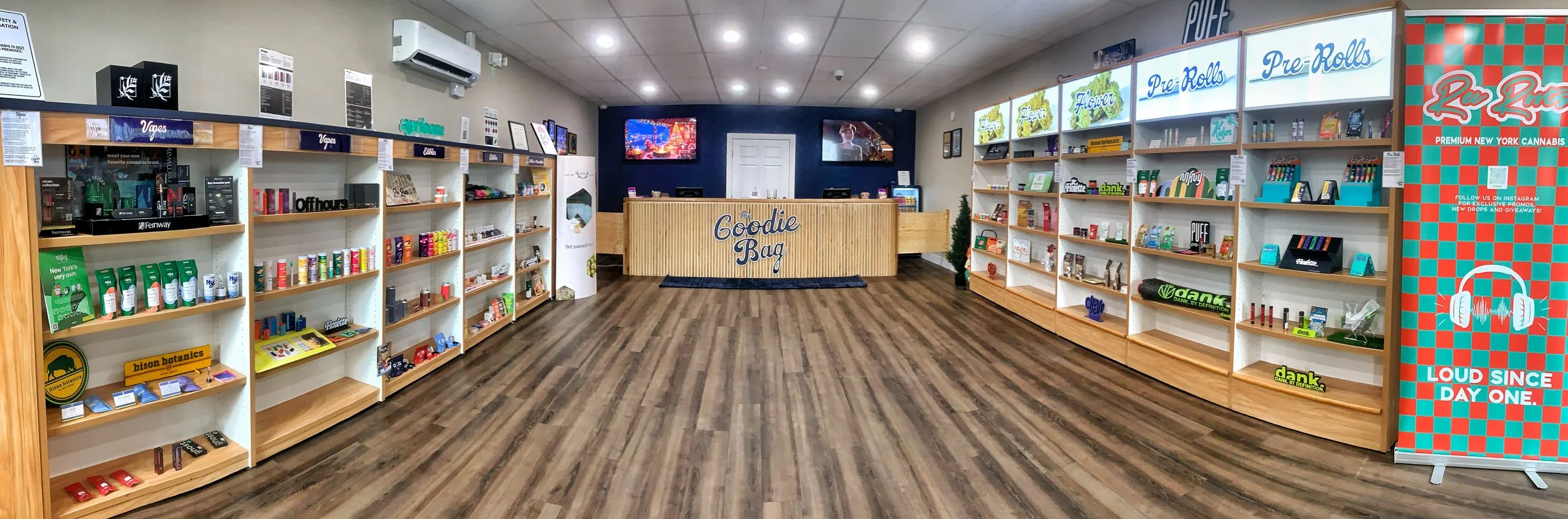 Interior of The Goodie Bag, a New York State Licensed Cannabis dispensary in Elmira, NY with shelves displaying various cannabis products, a checkout counter labeled 'Goodie Bag,' and promotional signage for pre-rolls, flowers, and vaping products.