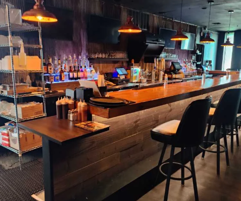 Bar counter with bar stools, liquor bottles, and bar equipment in a dimly lit restaurant or bar.