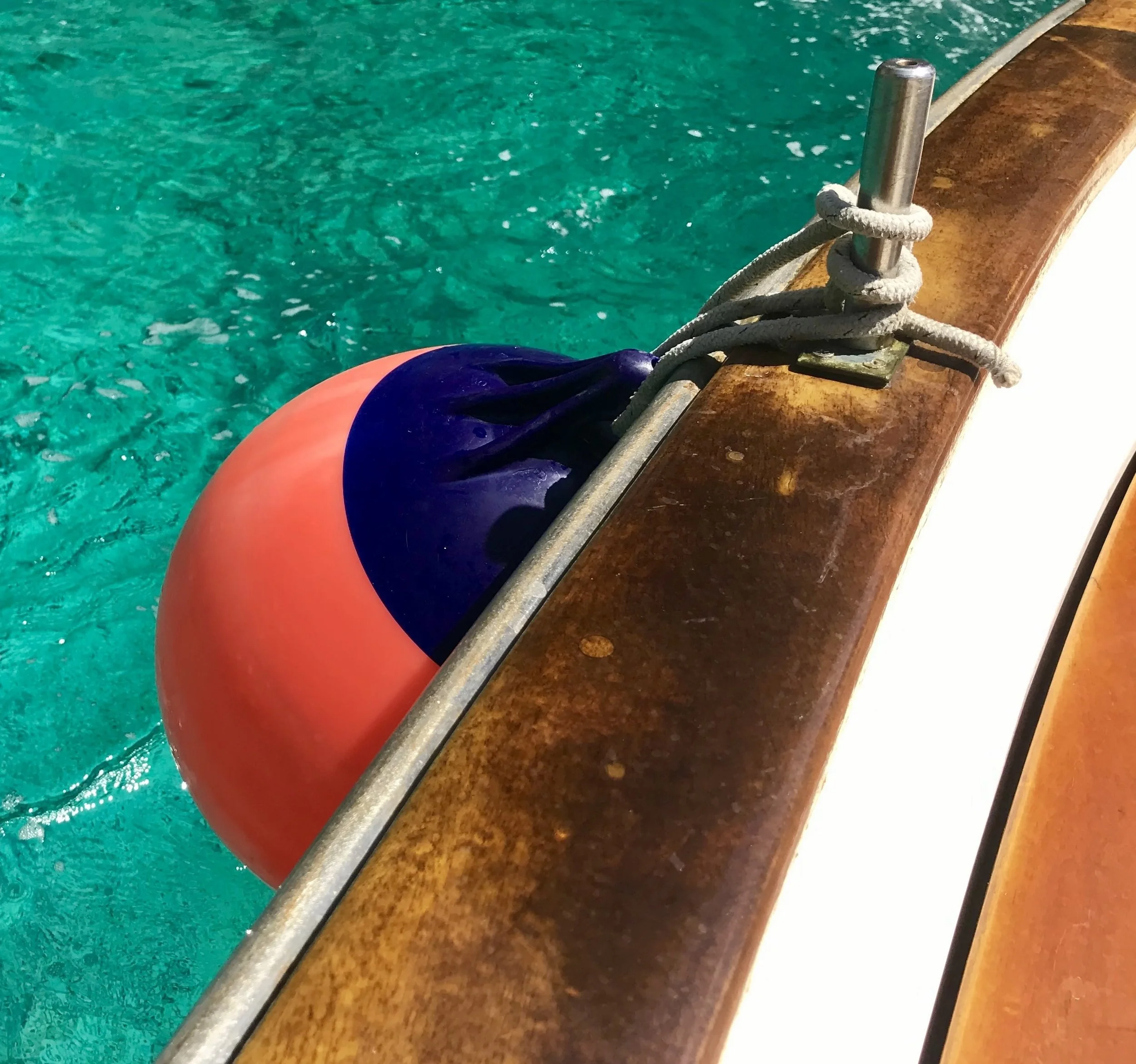 Close-up of a metal and wooden dock's edge with a white rope tied around a metal pole, next to turquoise swimming pool water.