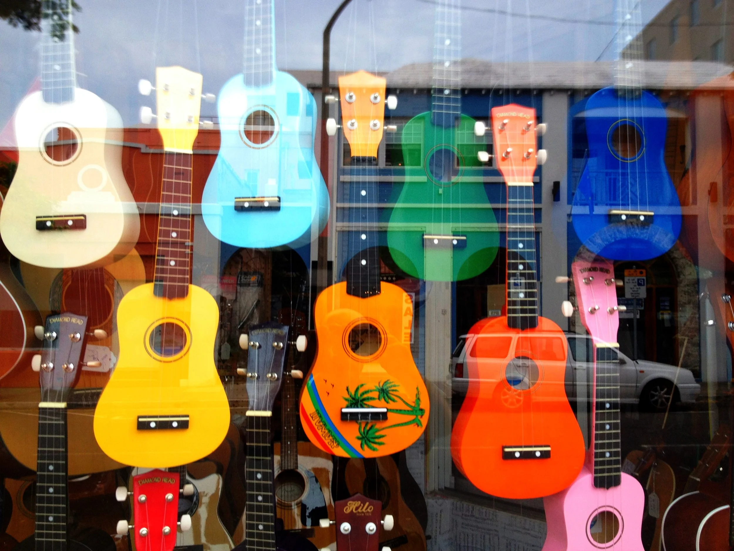 Display of various colorful ukuleles hanging in a shop window.