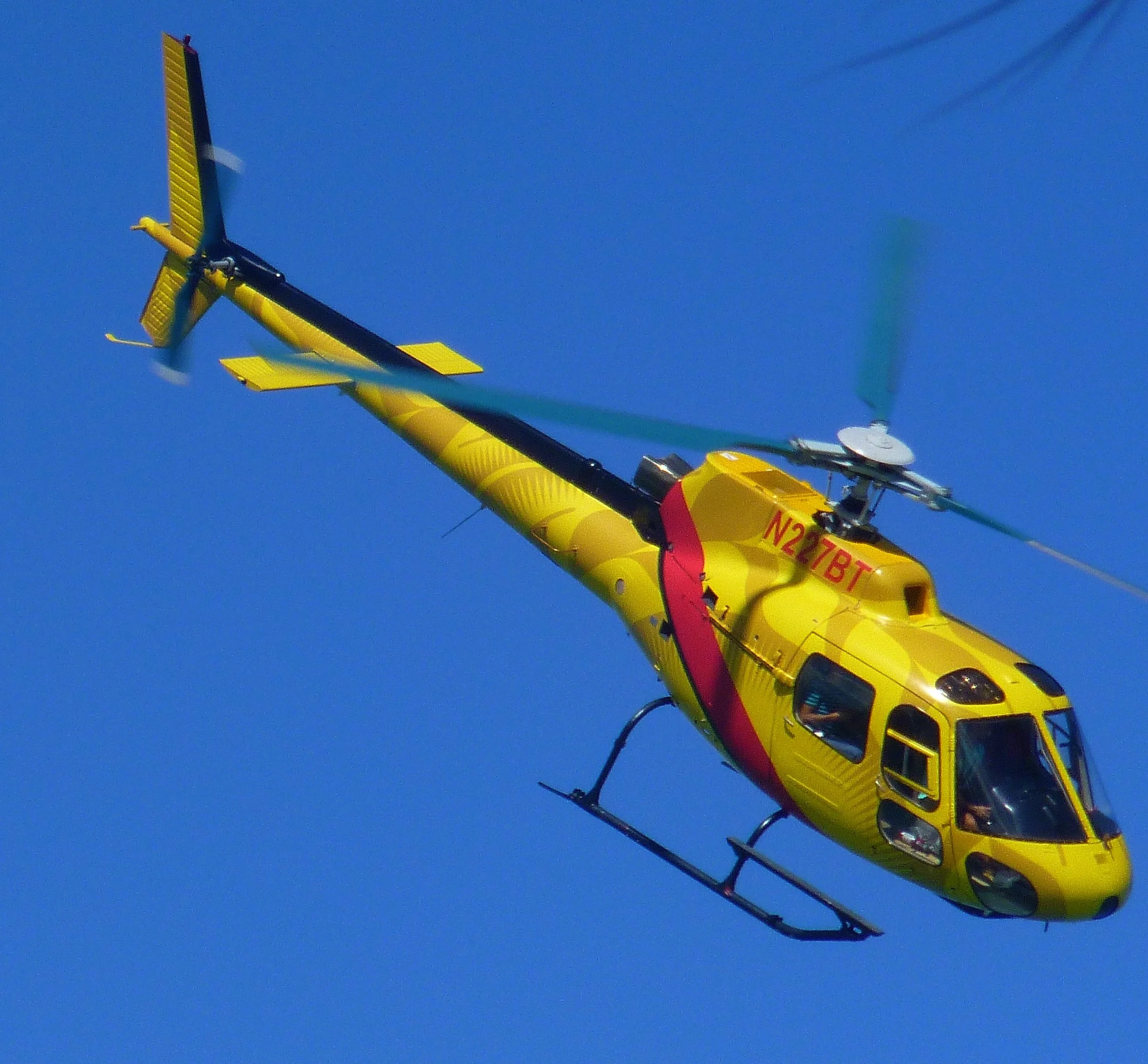 A yellow helicopter flying in the sky with blue background.