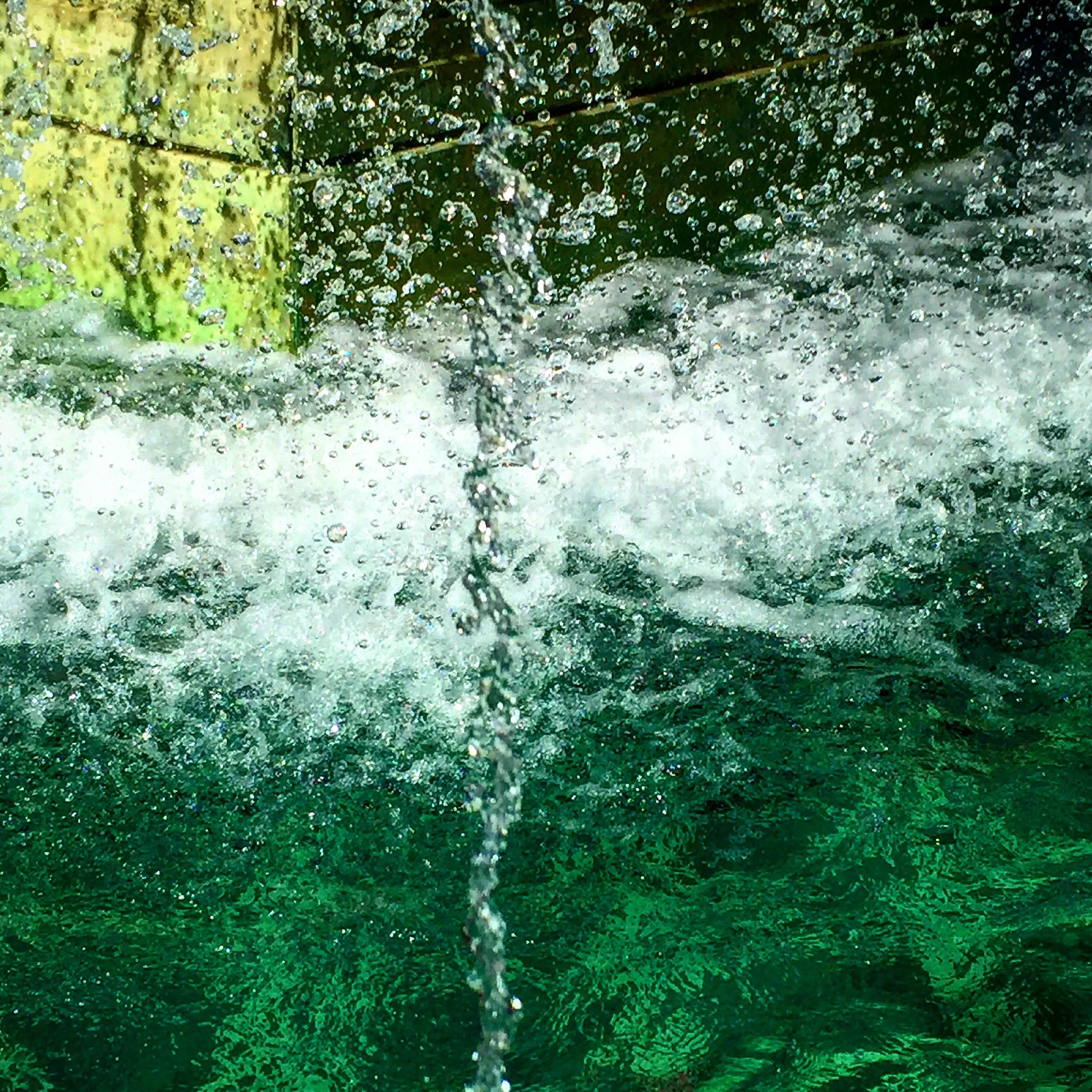 Close-up of a water fountain with bubbles, bubbles, and splashes surrounded by green foliage.