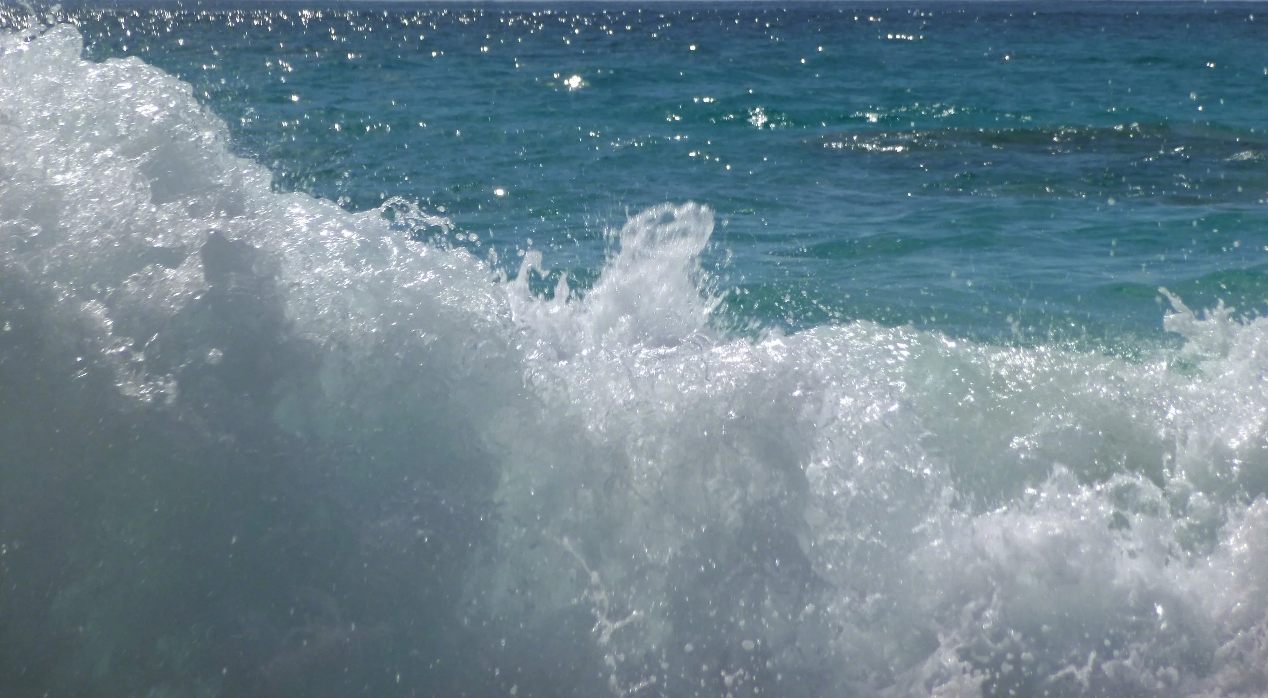Waves crashing in the ocean with foam and sparkling water under sunlight.