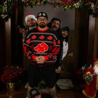 Group of five men standing in front of a decorated Christmas background, with one man in the front wearing a festive Naruto-themed sweater and a Santa hat.