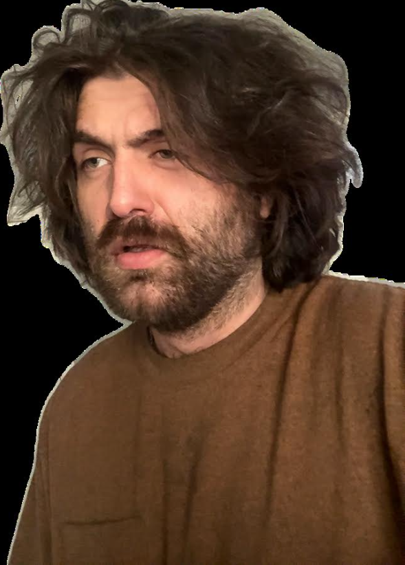 A man with messy brown hair and a beard wearing a brown sweater, looking slightly to the side.