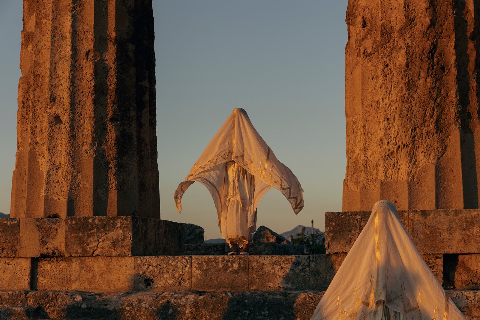 ANAMNESIS ceremonial performance by Apostolia Papadamaki among the columns of an ancient Greek temple at sunset.