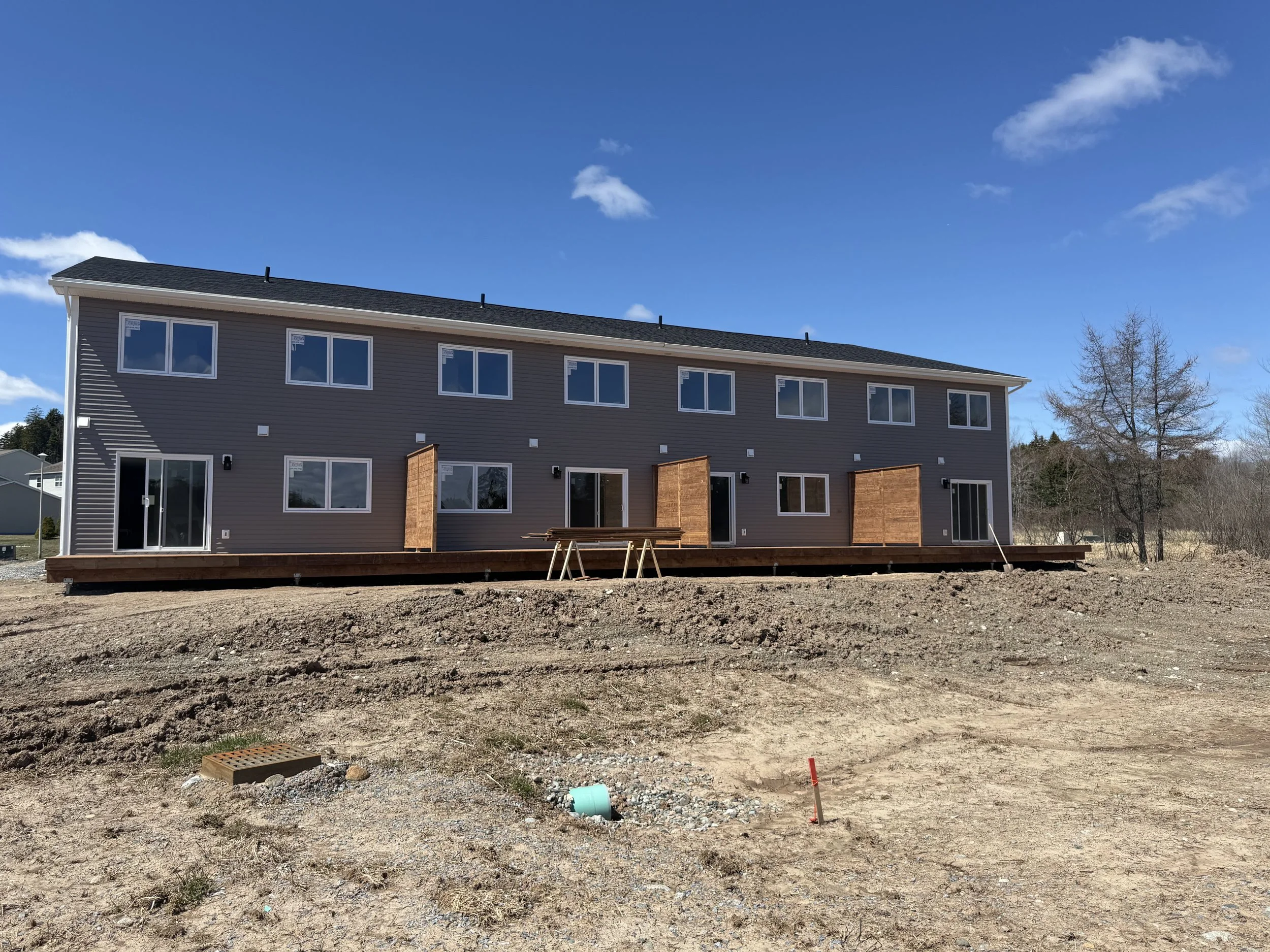 A row of newly constructed multi-story residential buildings in Saint John, NB with dark gray siding, large windows, and a black roof.