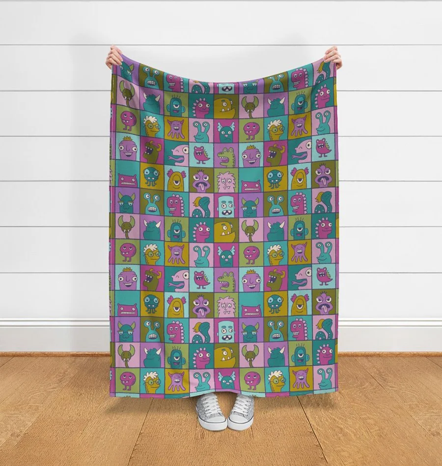 A brightly colored illustrated pattern of monster in individual boxes mocked up on a throw blanket