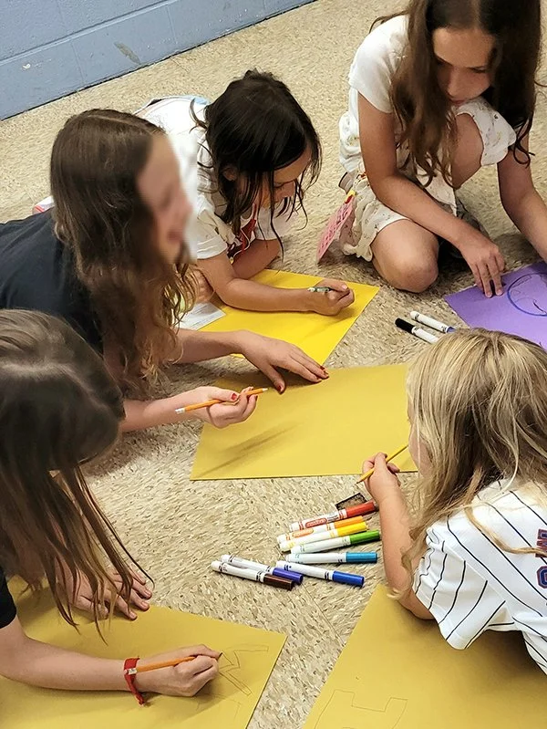 A group of kids lay on the floor drawing posters together