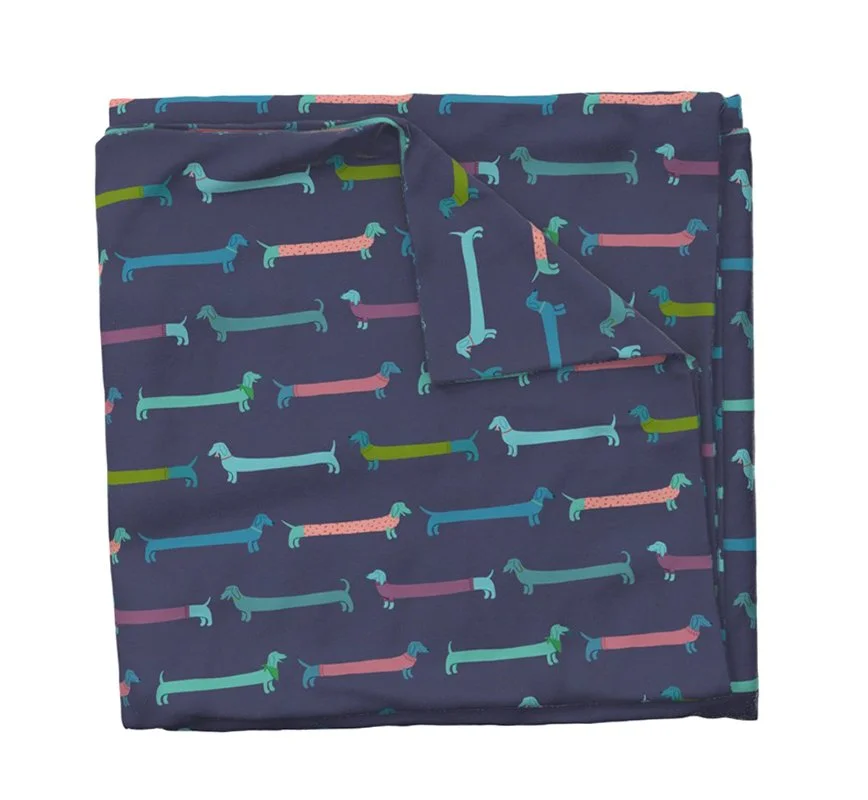 Mock-up of a tea towel with print featuring blue, purple, and teal dachshunds wearing sweaters and other accessories