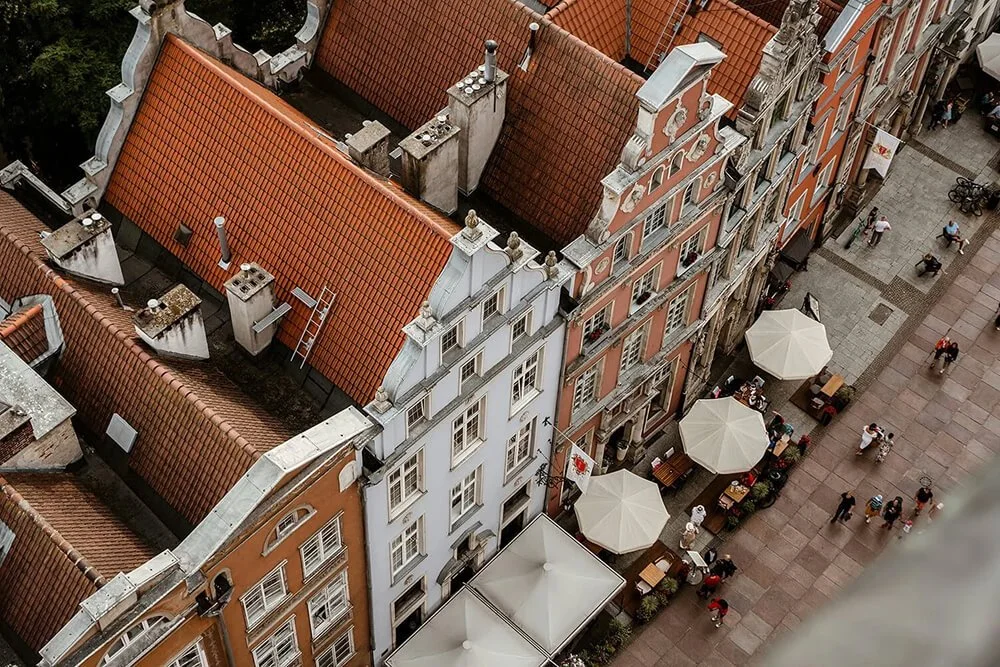 Aerial view of European-style buildings in Warsaw, Poland with red-tiled roofs and outdoor cafes on a cobblestone street.