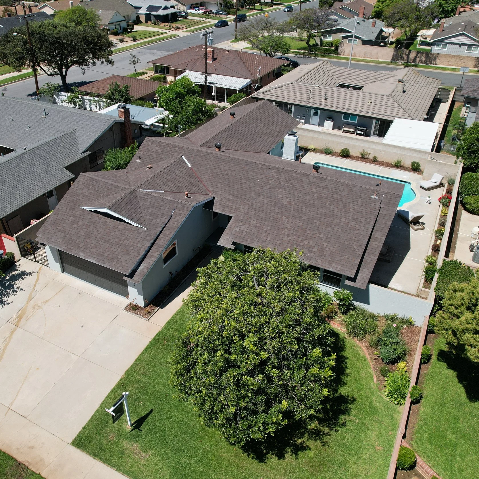 Aerial view of a suburban neighborhood showing houses, streets, trees, and a backyard with a swimming pool.