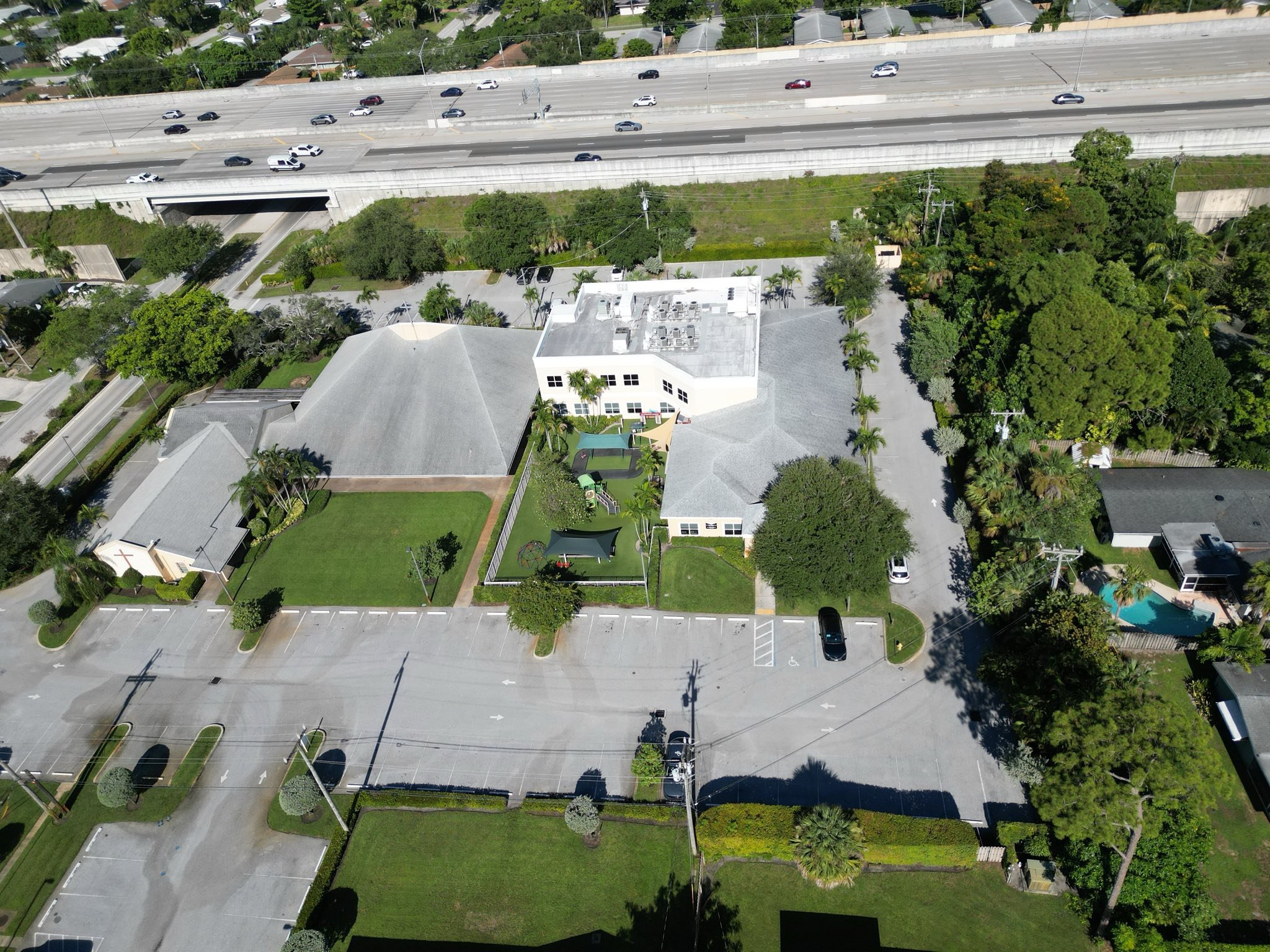 Aerial view of a residential area with multiple houses, a parking lot, and an interstate highway with cars passing overhead.