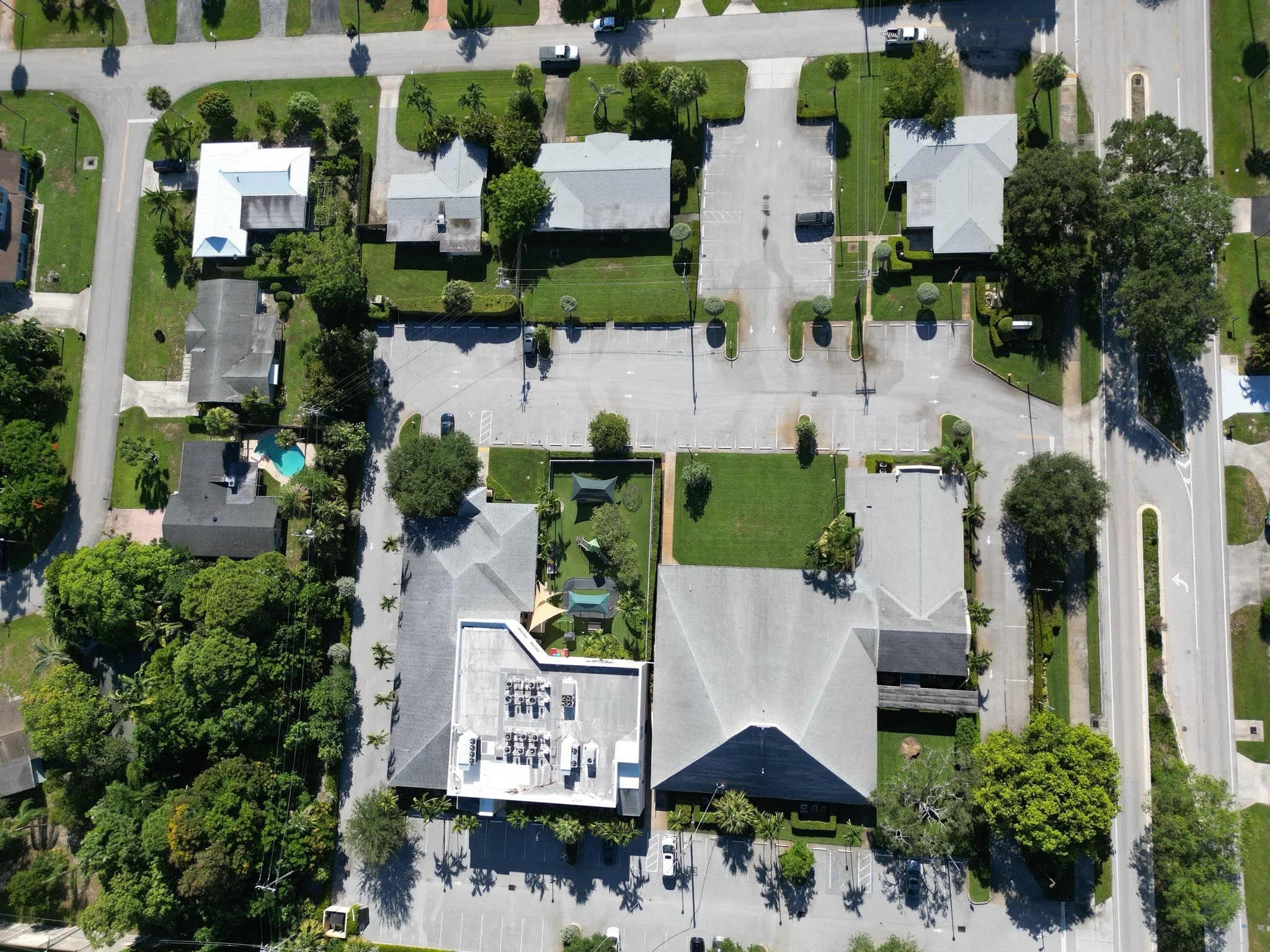 Aerial view of a residential neighborhood with green lawns, trees, houses, parking lots, and streets.
