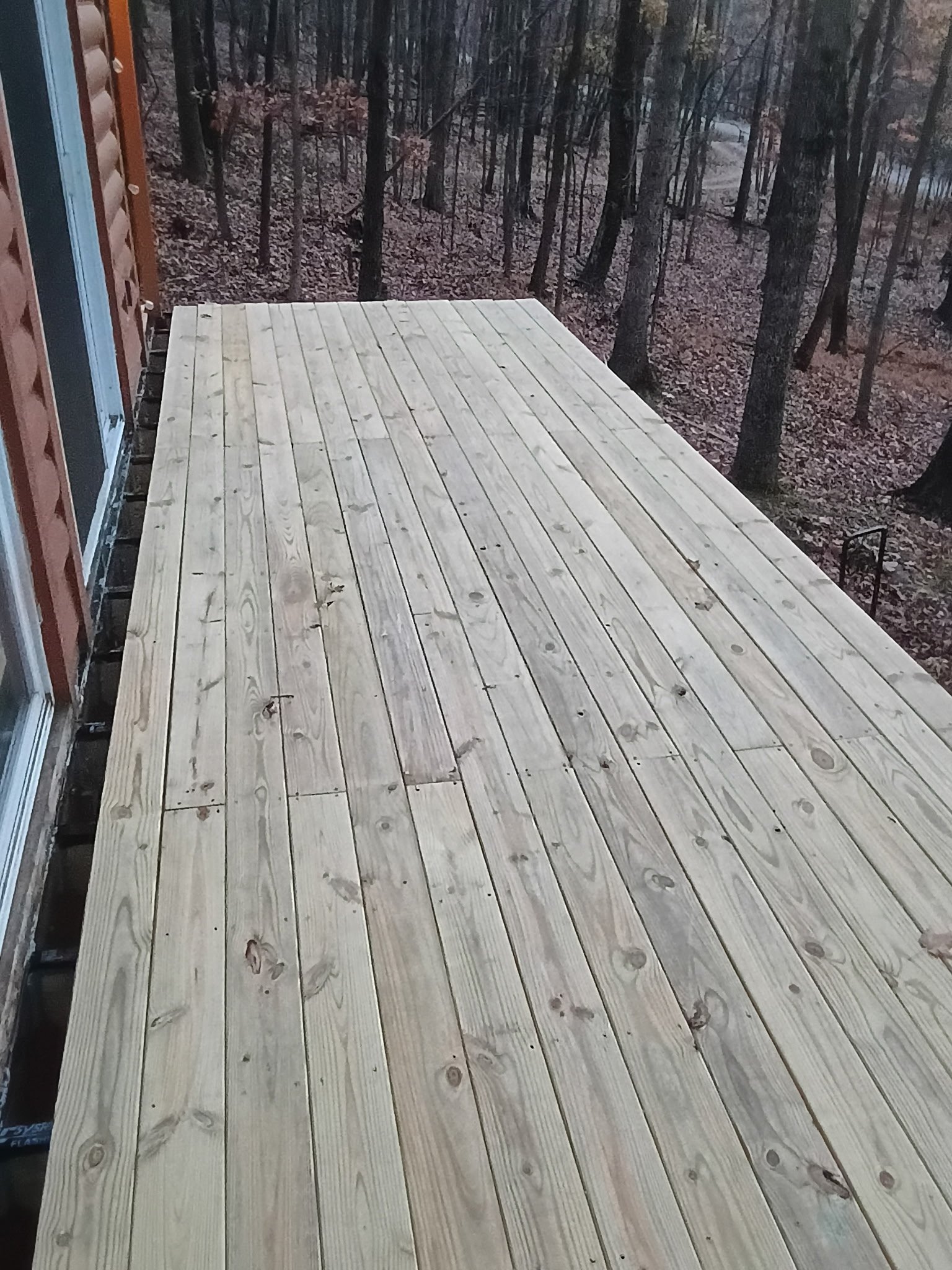 A newly built wooden deck attached to a house with a forest background.