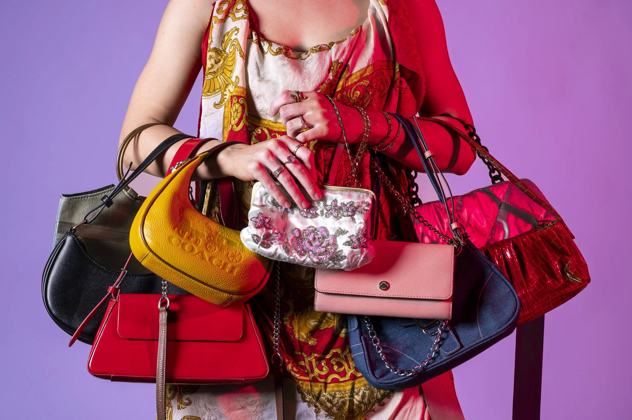 Person wearing a colorful dress with multiple handbags hanging from their arms, with a purple gradient background.