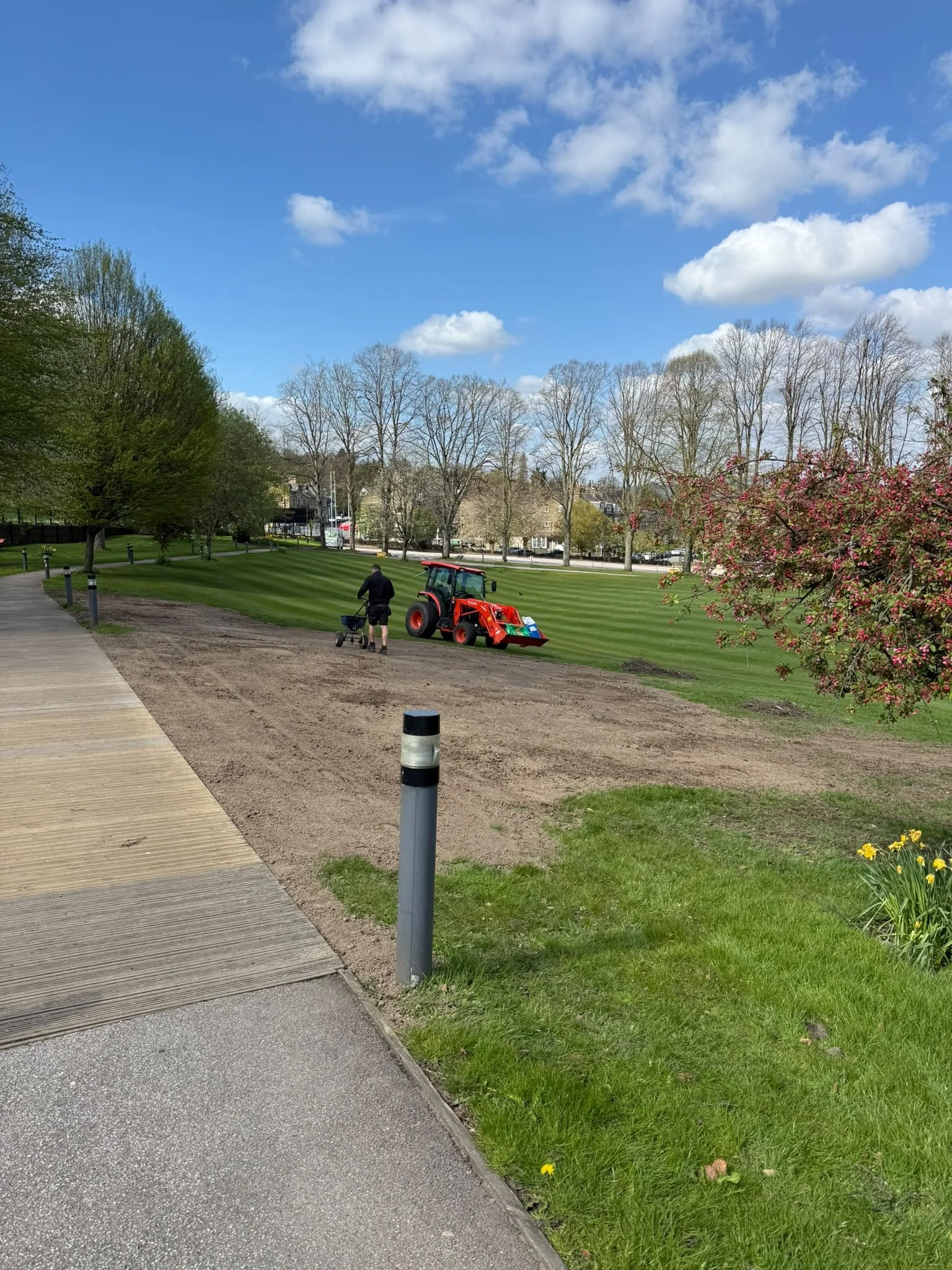 Operator seeding prepared ground beside a tractor and established lawns