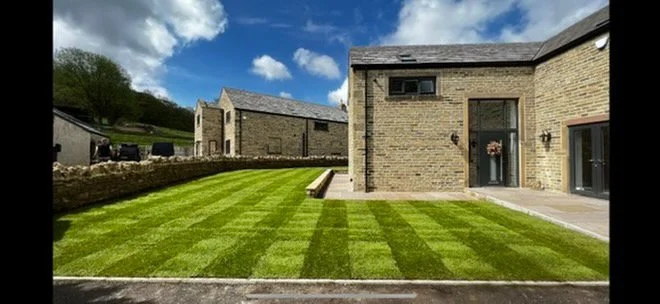 Striped natural turf lawn beside a stone house and patio