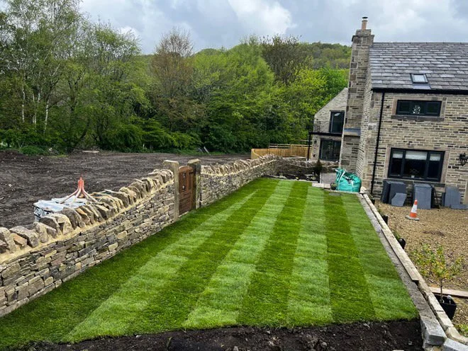 Freshly laid turf beside a dry-stone wall and stone house